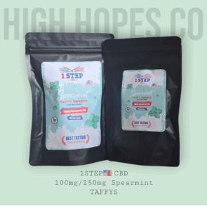 lose-up of two 1STEP CBD Spearmint Taffy Sweets packages. The left package shows 250mg full spectrum CBD (10mg per sweet), while the right displays 100mg full spectrum CBD (10mg per sweet). Both feature a sleek black design with green and white accents and spearmint leaves, with 'HIGH HOPES CO' in large light green letters in the background and '1STEP CBD 100mg/250mg Spearmint TAFFYS' at the bottom."